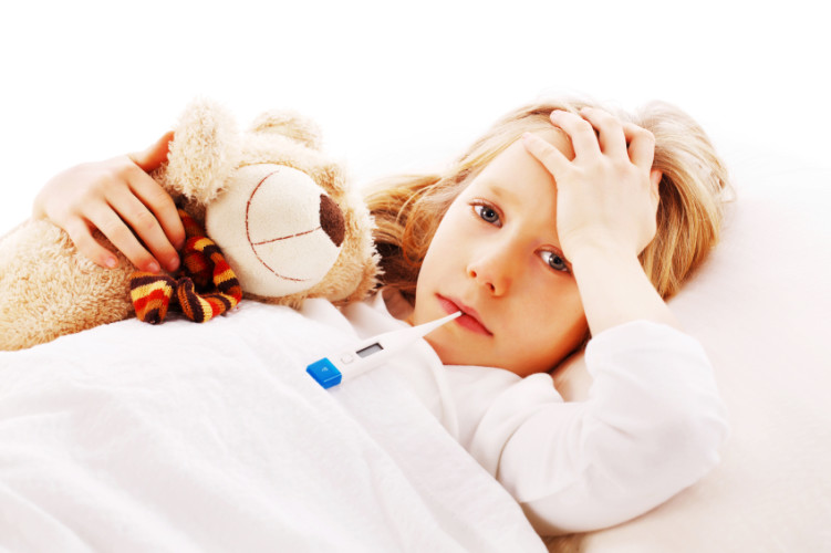 Little girl lying sick in her bed with her teddy bear.
